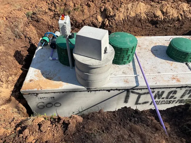 Concrete aerobic tank with control panel and green lids being set in the ground