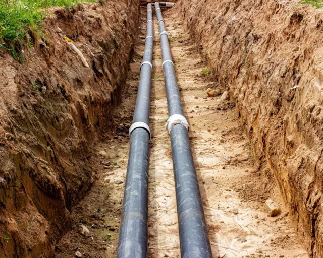 Two pipes run side by side in a trench