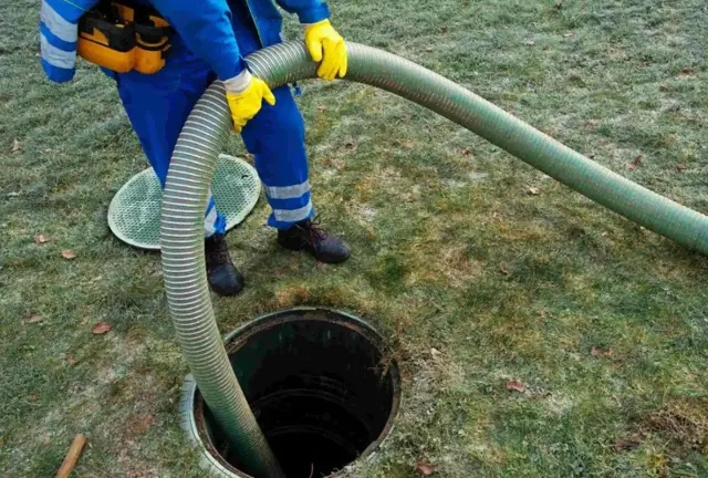 Technician pumping a septic tank with a vacuum hose