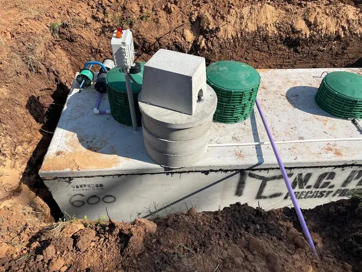Concrete aerobic tank with control panel and green lids being set in the ground