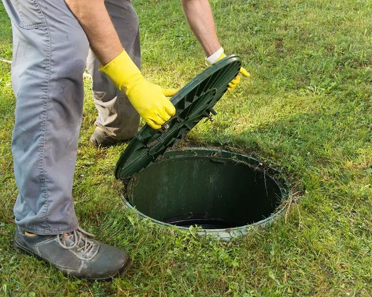 Technician lifting a green septic tank lid (tank lid glossary guide)