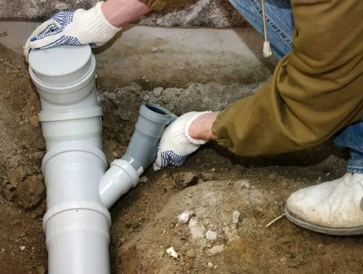 Gloved hands fitting PVC drain pipe in an excavation (cleanout glossary guide)