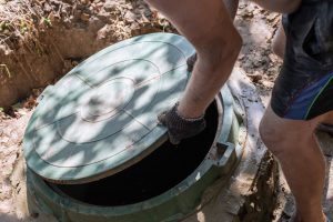 The man opens the sewer hatch. Installation and maintenance of septic tanks.