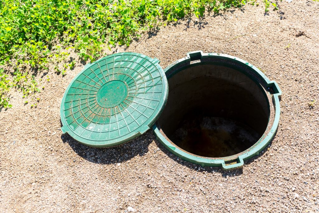 Opened unsecured sewer manhole of rural septic tank with green plastic cover